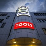 Ljuslåda för TOOLS med röd bakgrund och vit text monterad på byggnadsfasad.
